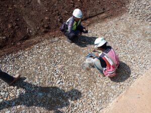 Dua orang tim dari PT BBSP mengenakan helm dan rompi keselamatan sedang melakukan pengujian kualitas material agregat di lokasi proyek pembangunan Tol Akses Patimban.