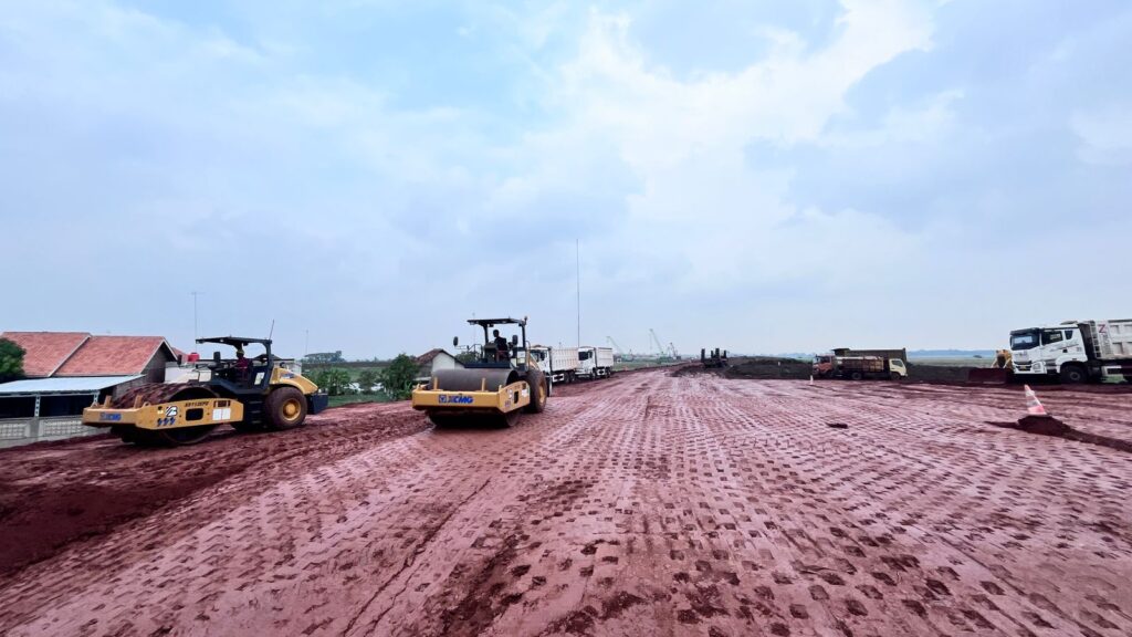 memadatkan lapisan tanah merah pada dasar jalan di lokasi pembangunan Proyek Tol Akses Patimban