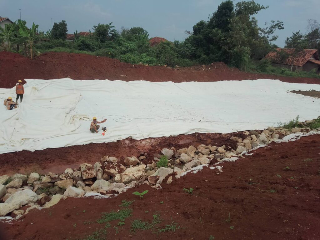 Pekerja PT BBSP sedang memasang dan merapikan lembaran geotekstil putih di lereng tanah merah Proyek Tol Akses Patimban