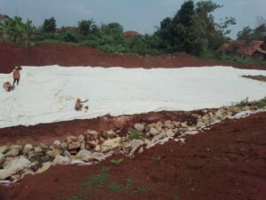 Pekerja PT BBSP sedang memasang dan merapikan lembaran geotekstil putih di lereng tanah merah Proyek Tol Akses Patimban